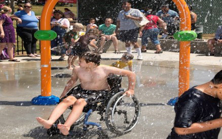 kid in wheelchair playing on splash pad